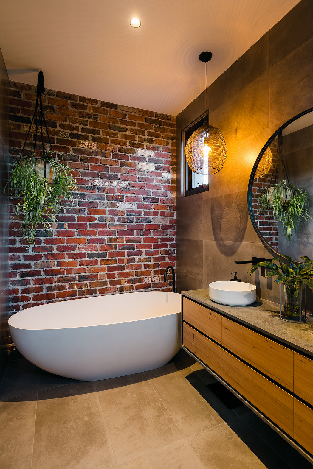Rustic brick walls, modern bathtub, wood vanity, and stylish lighting create a cozy bathroom.