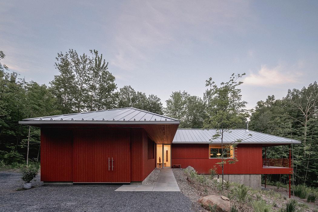 A rustic, red-wood modern cabin nestled in a lush forest with a sleek metal roof.