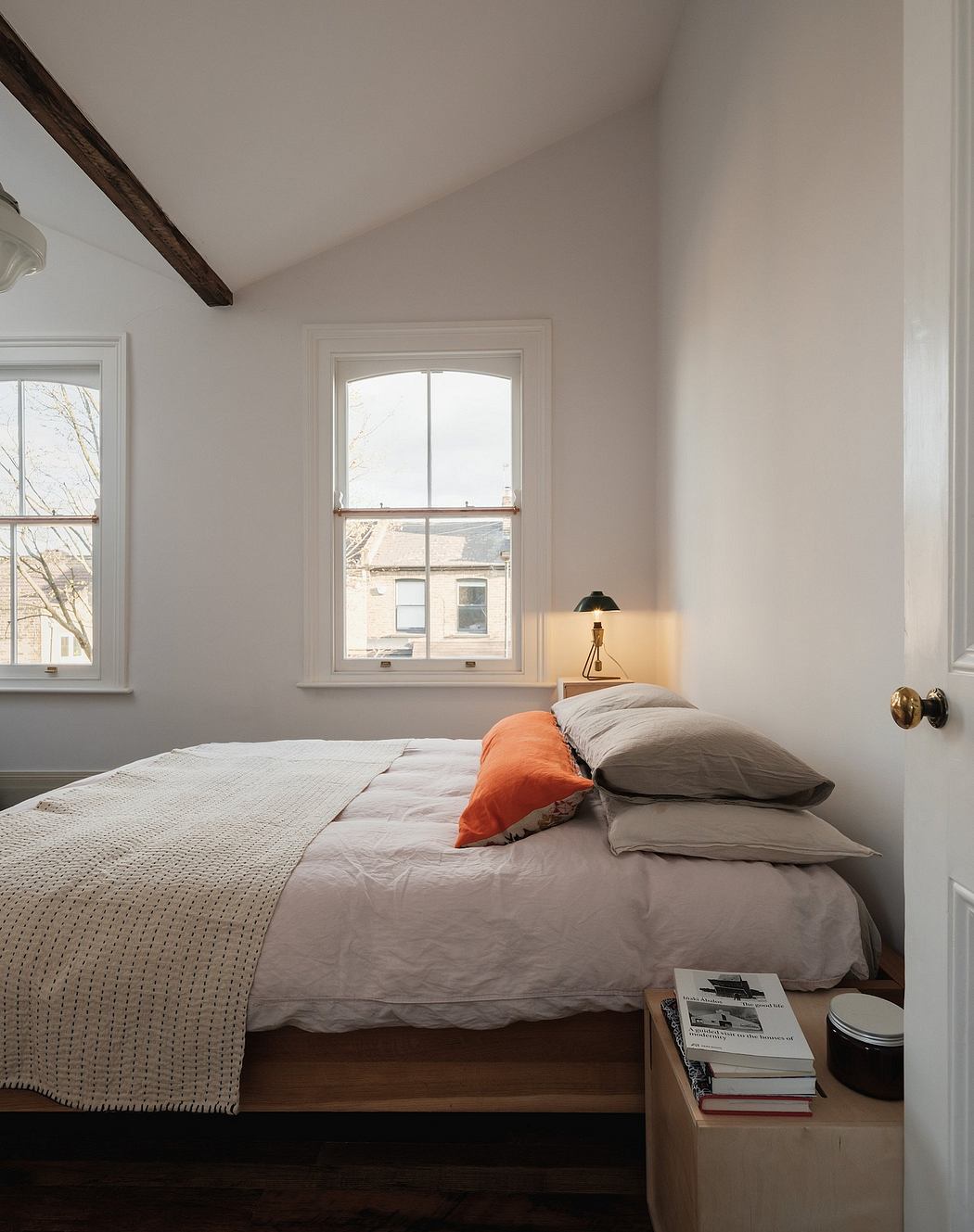 Cozy bedroom with arched window, exposed wooden beams, and neutral tones.