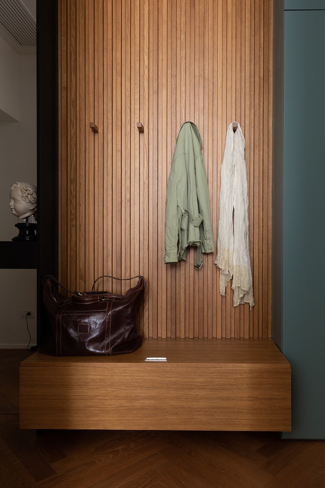 A modern entryway with a wooden wall, hanging coats, and a leather bag on a wooden bench.