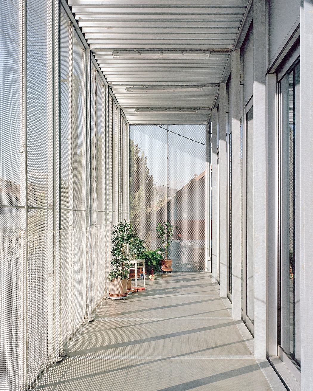 Expansive, glass-enclosed corridor with metal grille walls and potted plants along the floor.