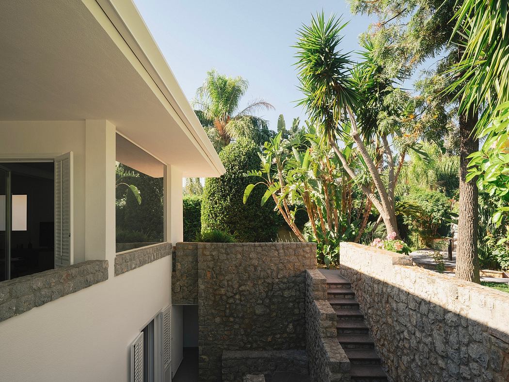 A modern villa with a stone facade, surrounded by lush tropical plants and trees.