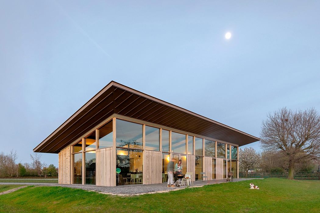 A modern wooden and glass structure with a slanted roof stands in a grassy field.