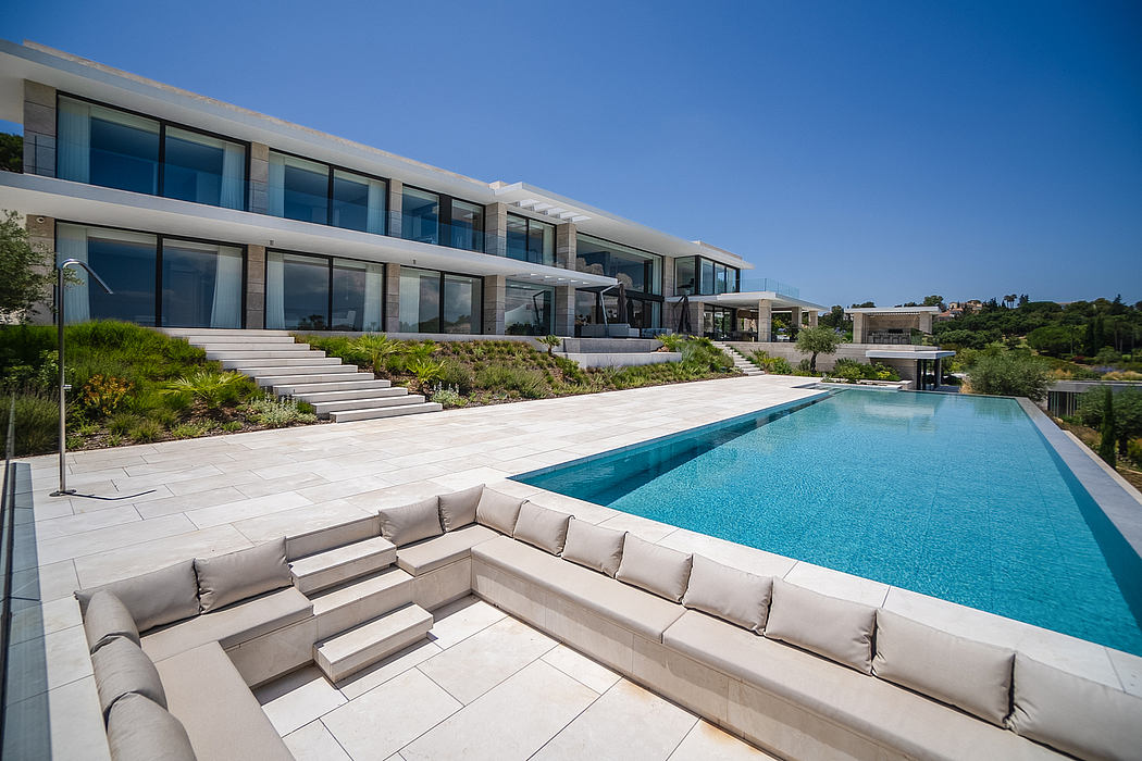 Sleek, modern villa with expansive, glass-walled structure, infinity pool, and lush landscaping.