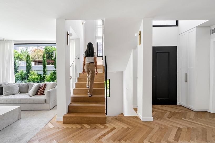 Minimalist modern entryway with wooden stairs, white walls, and large windows overlooking greenery.