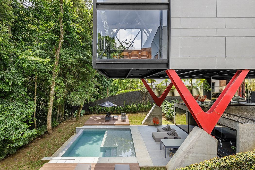 Modern home with glass walls, red architectural elements, and a pool in a lush, forested setting.