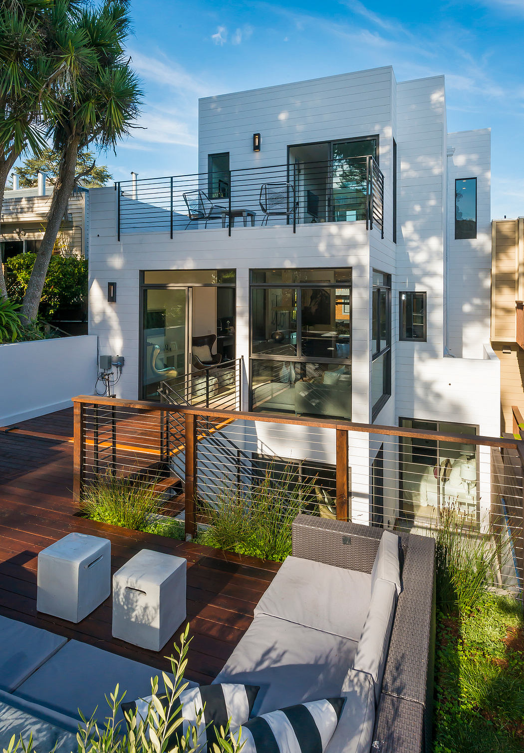 Contemporary two-story home with sleek exterior, expansive deck, and lush landscaping.