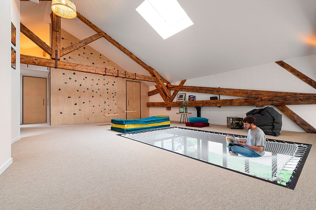 A spacious attic loft with exposed wooden beams, colorful furnishings, and a person working on a laptop.