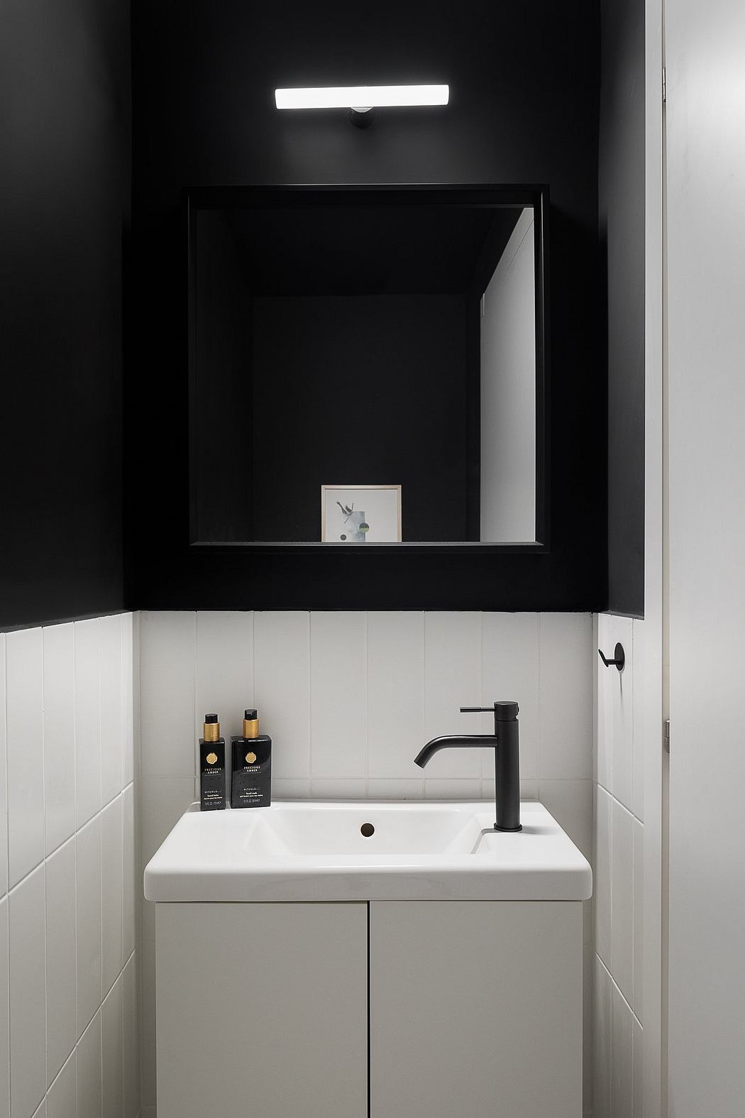 Minimalist bathroom with black wall, white vanity, and modern lighting fixture.