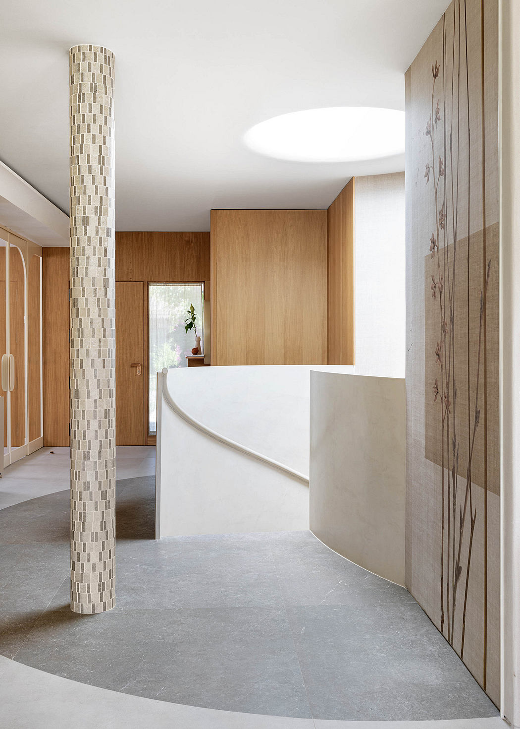 A modern, minimalist foyer with a tiled column, wood cabinets, and a curved concrete reception desk.