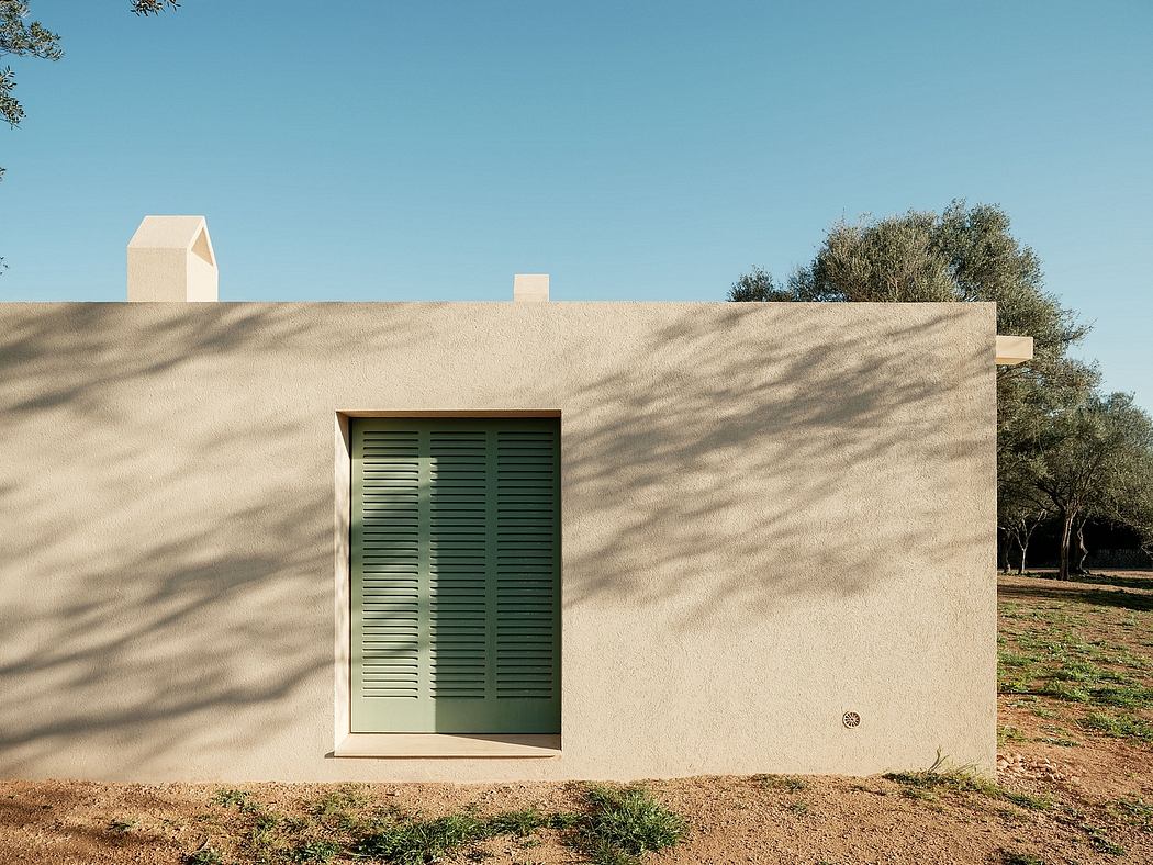 A minimalist building with a green, louvered door and geometric accents against a sandy exterior.