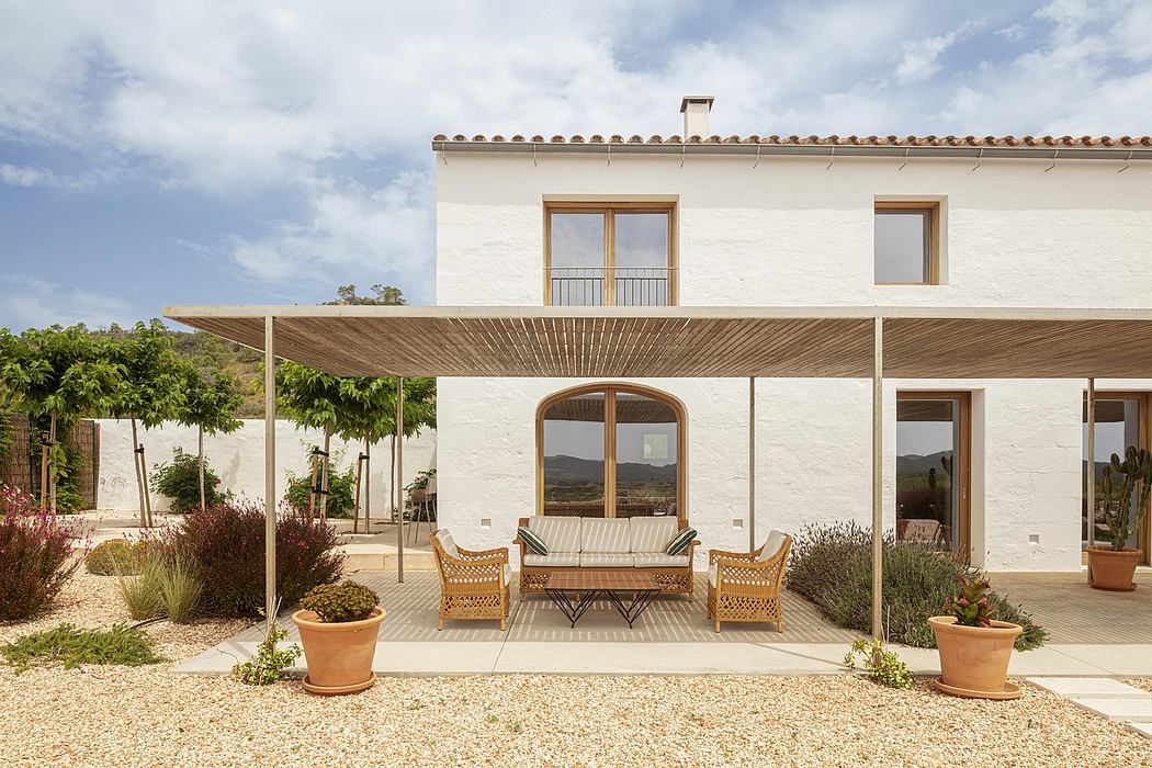 A modern rustic villa with a covered patio, wooden furnishings, and potted plants.