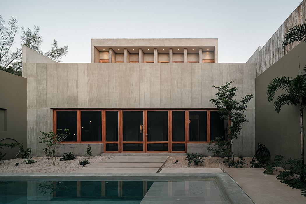 Minimalist concrete structure with wooden windows and doorways, surrounded by lush vegetation.
