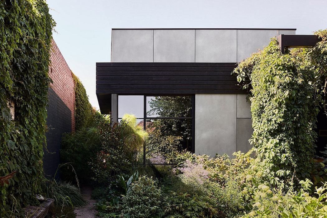 A contemporary, minimalist building with bold black lines framed by lush, verdant foliage.
