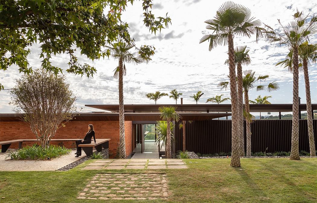 A modern building with a brick exterior, tall palm trees, and a paved path leading to the entrance.