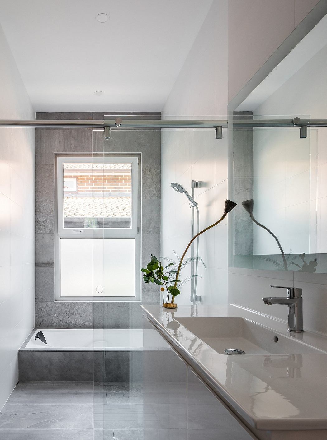 Modern bathroom with gray tile, sliding glass doors, and a potted plant on the counter.