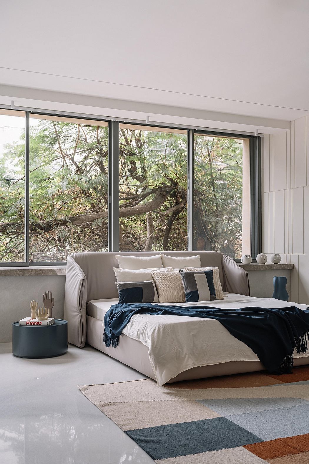 Cozy bedroom with floor-to-ceiling windows overlooking lush greenery; modern, neutral decor.