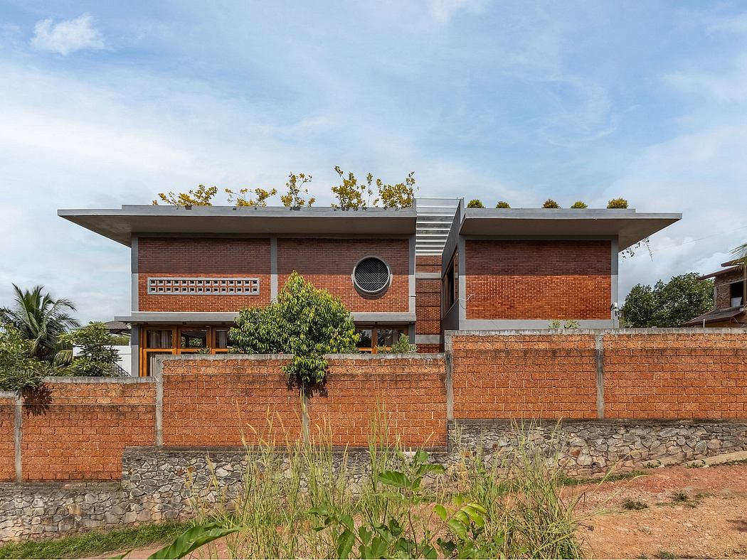 A modern brick home with a flat roof, surrounded by vegetation and stone walls.
