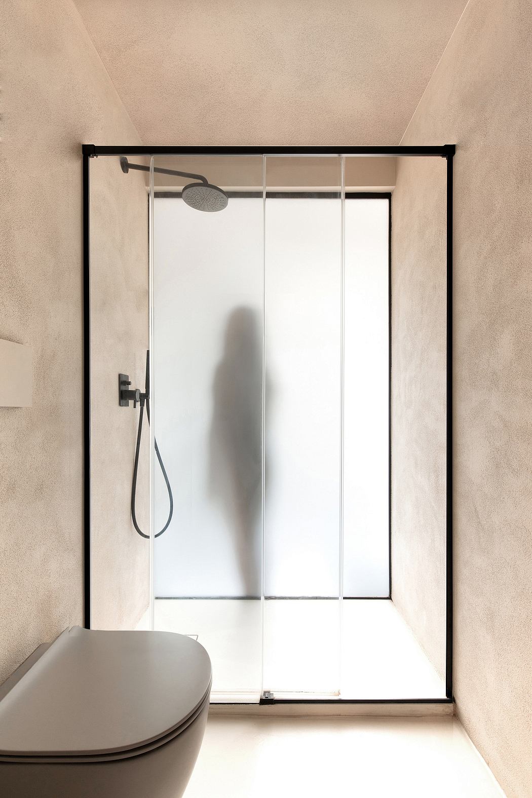 Minimalist bathroom design with glass shower enclosure and black metal frame.