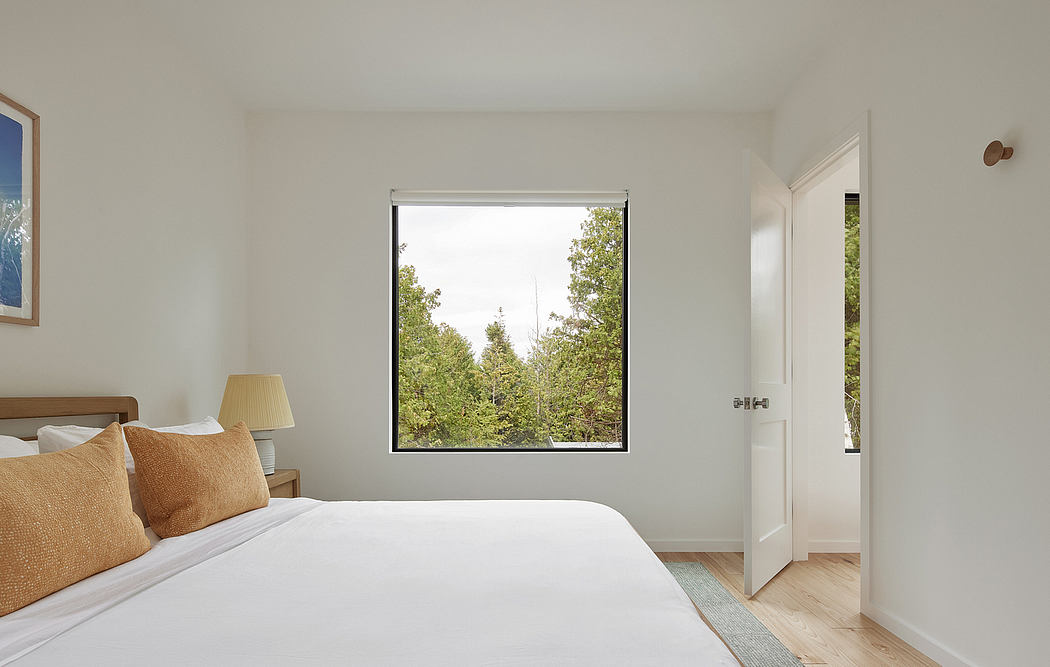 Spacious bedroom with large window offering serene forest view, minimalist decor.