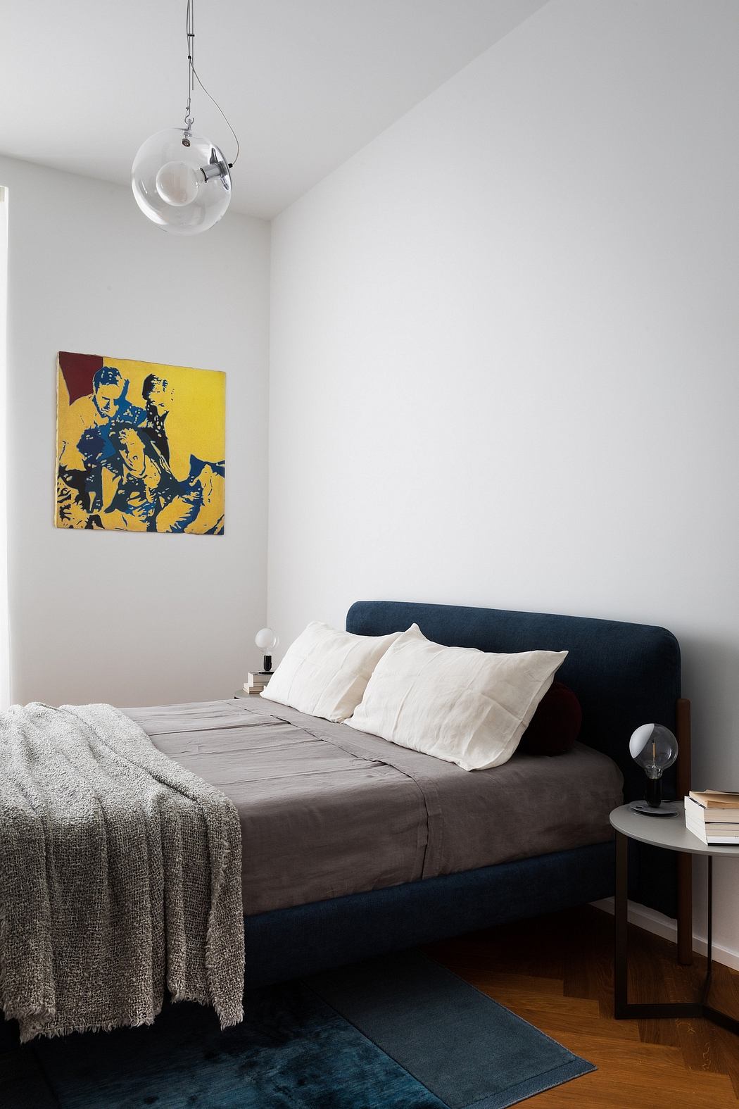 Modern minimalist bedroom with bold pop art print, a dark blue bed frame, and globe lighting fixture.