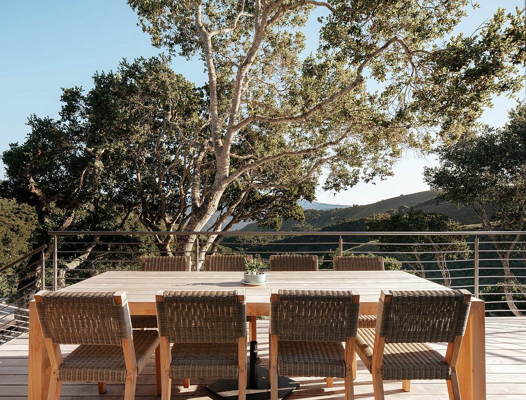 A modern outdoor dining area with a large wooden table, woven wicker chairs, and a stunning natural backdrop.