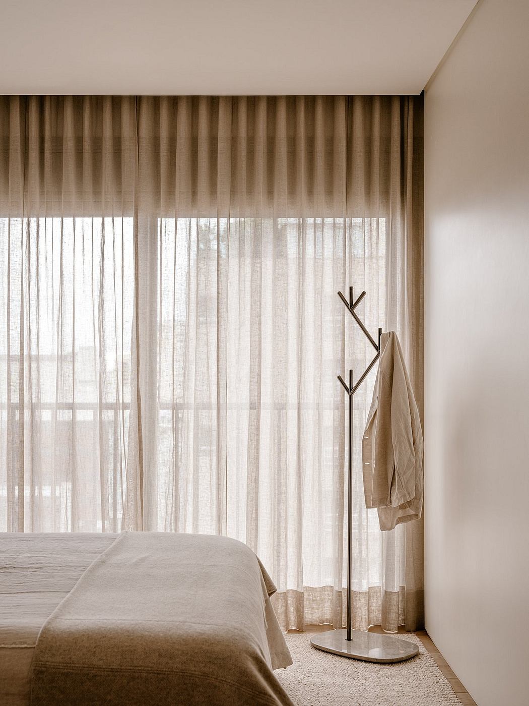 A cozy bedroom with neutral tones, sheer curtains, and a modern coat rack.