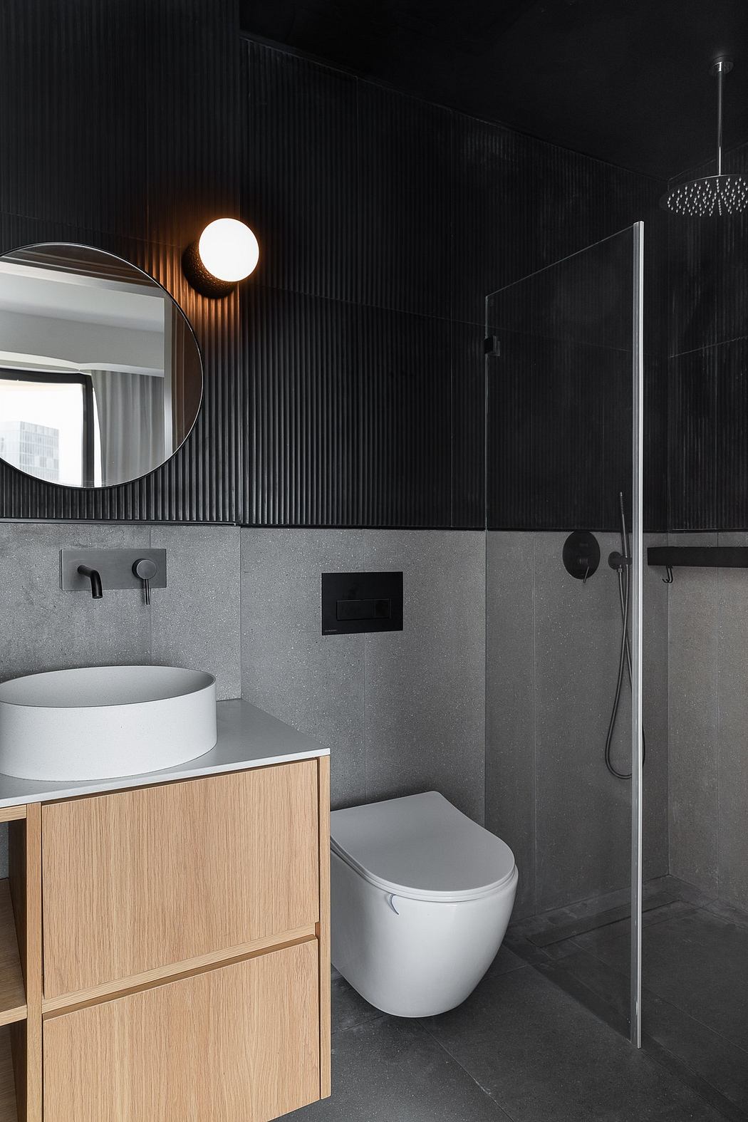 Minimalist bathroom design with wood vanity, white sink, and dark tiled walls.