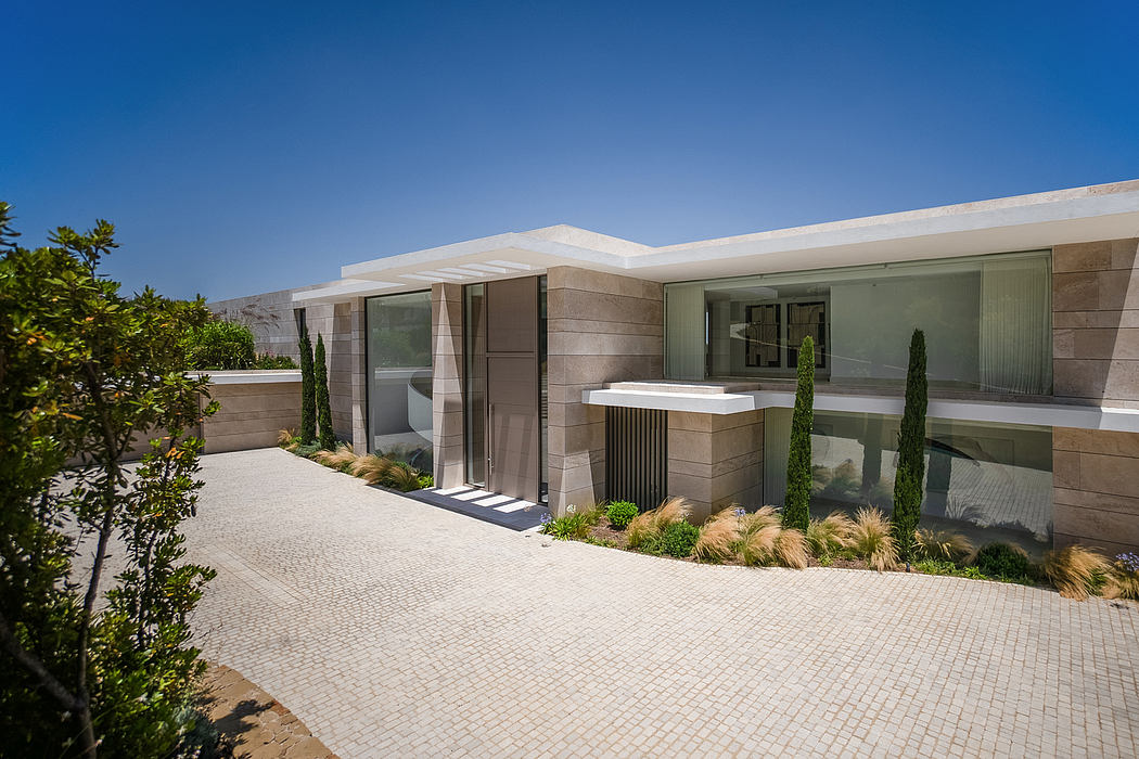 Modern beige stone exterior with glass walls, pavement, and landscaped greenery.