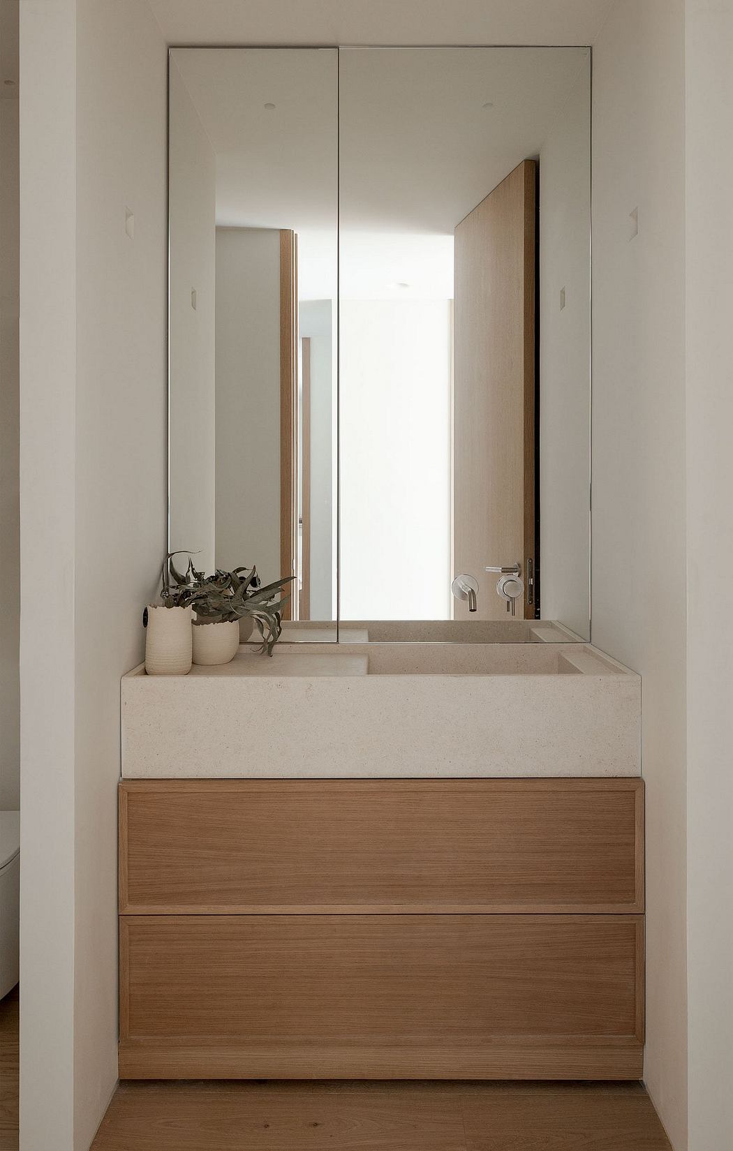 Minimalist bathroom vanity with concrete sink basin, wood drawers, and mirrored cabinets.