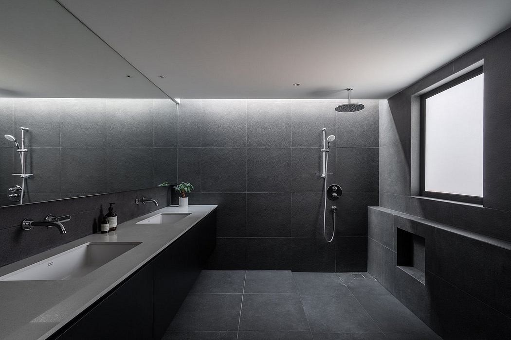 Modern, minimalist bathroom with sleek black tiles, double vanity, and rain shower.