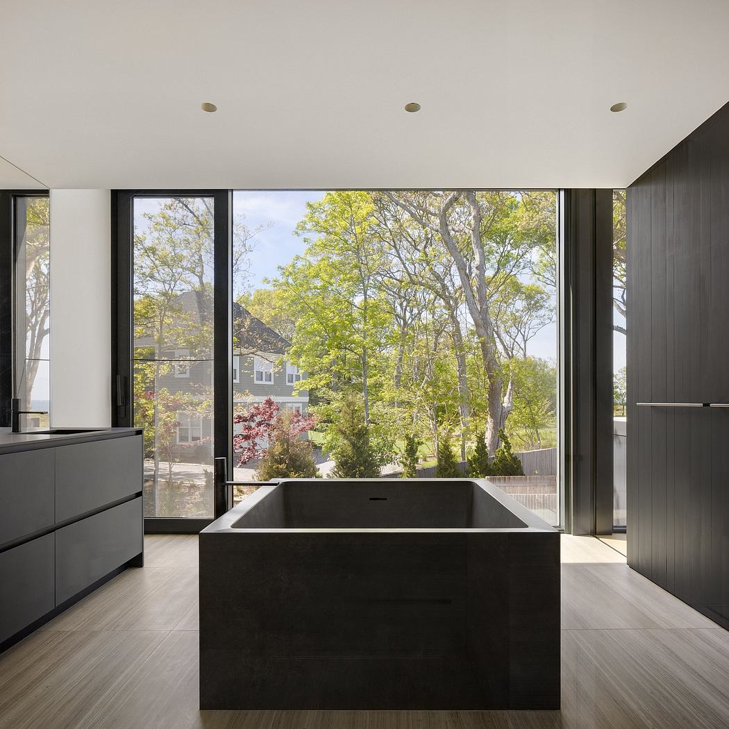 Sleek modern kitchen with black cabinetry and large windows framing lush outdoor greenery.