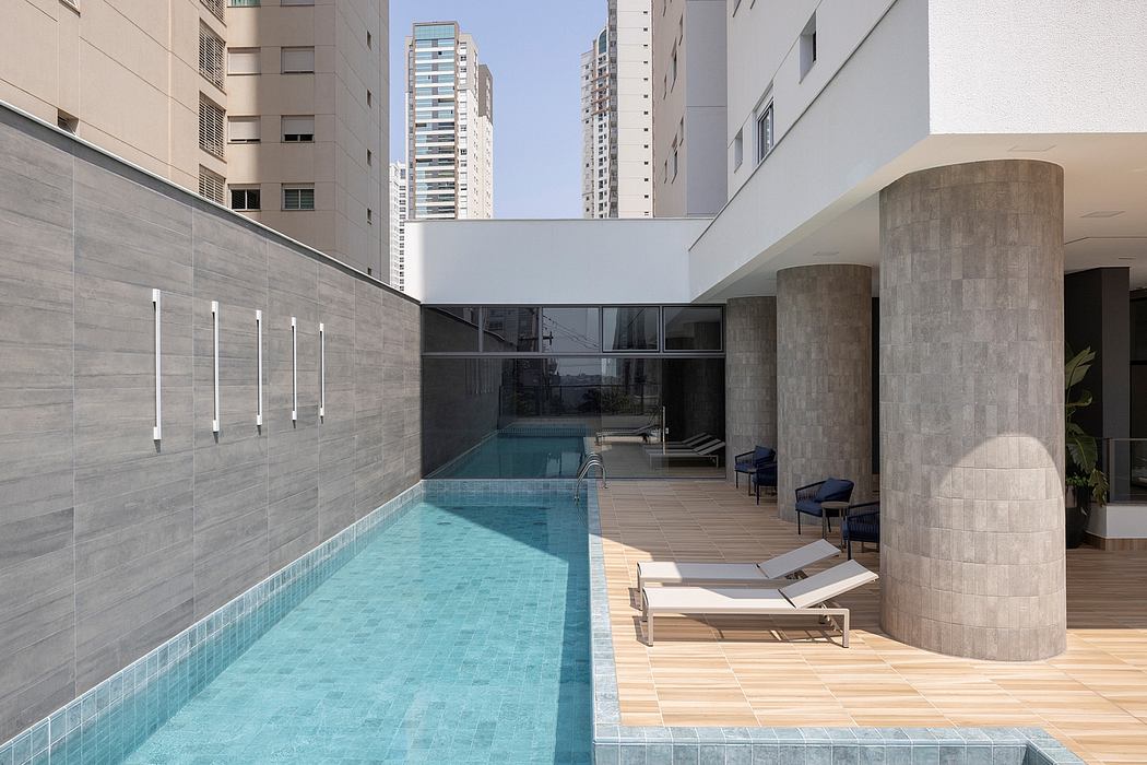 Sleek, modern apartment building with a lap pool, lounge chairs, and minimalist architecture.