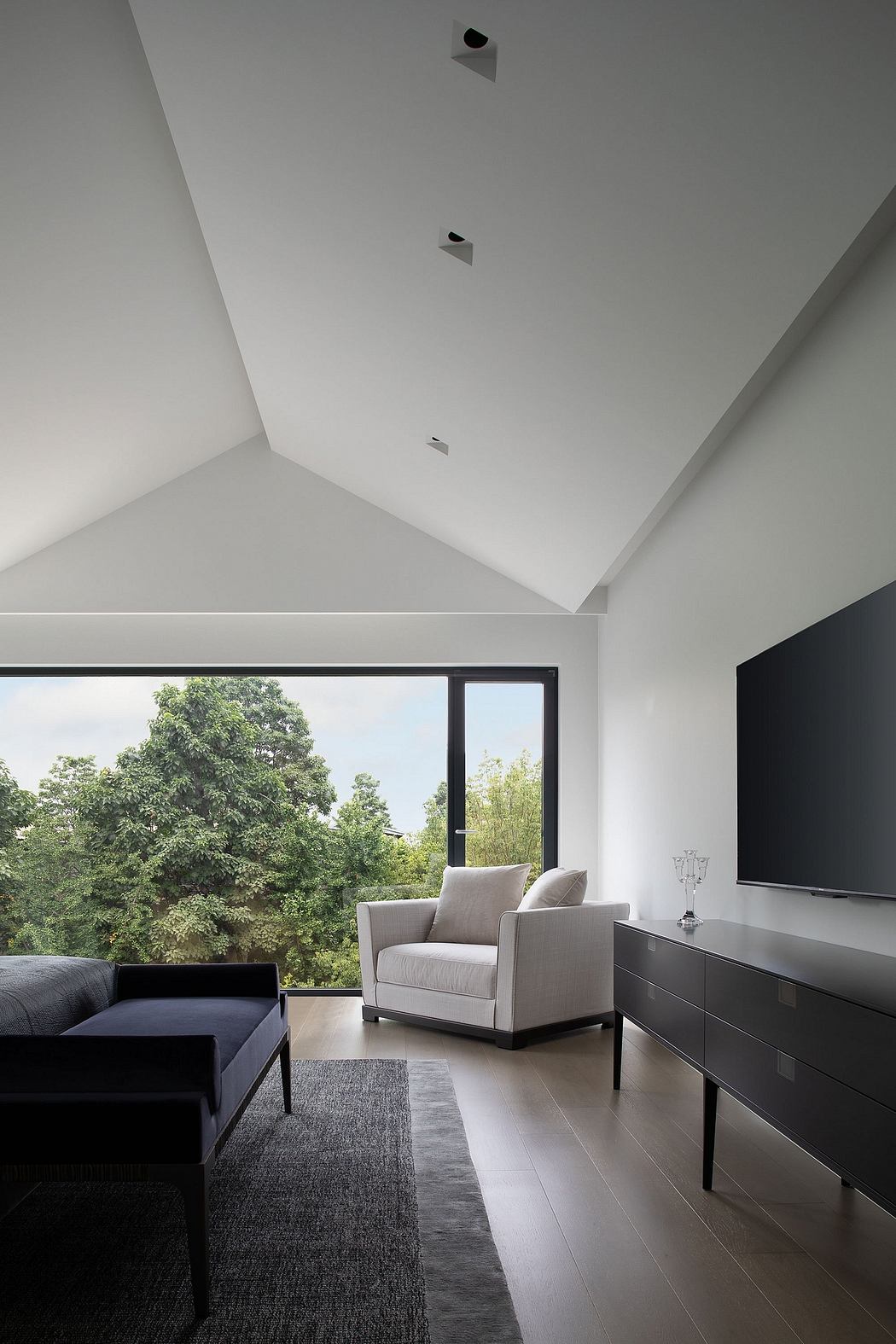 Minimalist living room with large windows overlooking lush greenery, sleek furniture, and recessed lighting.