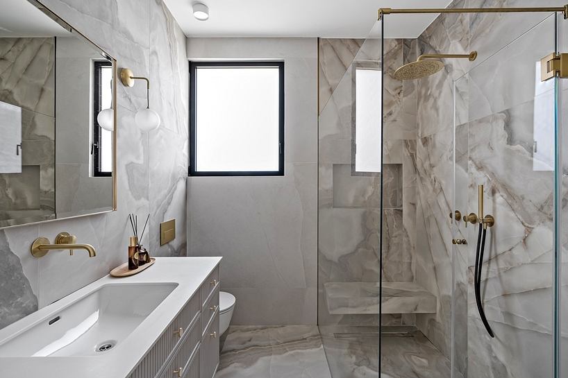 Spacious bathroom with marble-look tiles, gold fixtures, and a large window.