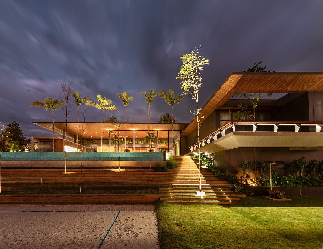 A modern, wood-paneled building with a covered patio, steps, and lush landscaping at night.