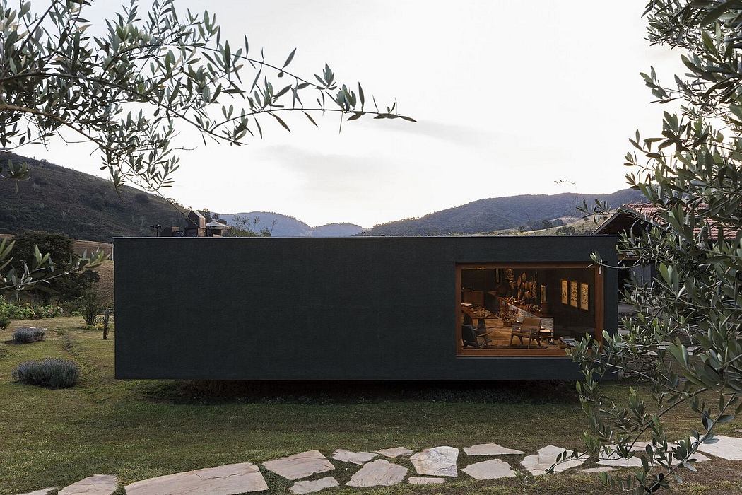 A modern, dark-colored home set amid a lush, mountainous landscape, with large windows providing a scenic view.