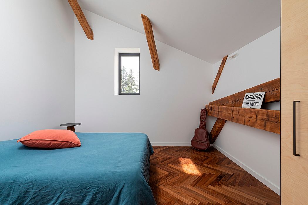 Cozy attic bedroom with exposed wood beams, built-in shelving, and herringbone wood floor.
