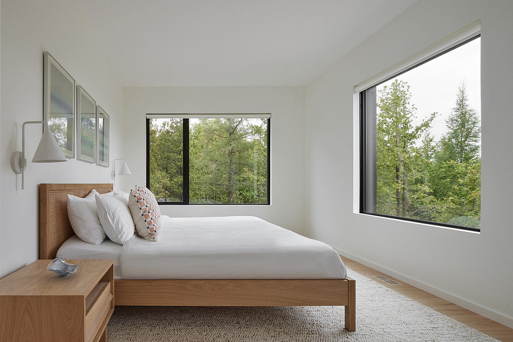Minimalist bedroom with large windows overlooking lush foliage, wooden frame bed, and cozy rug.