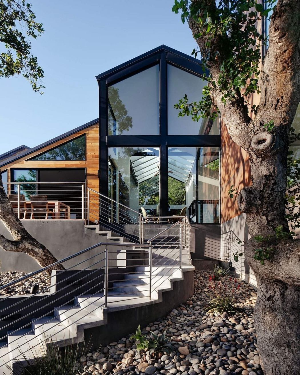 A contemporary glass-enclosed structure nestled among trees, with a wooden exterior and sleek metal railings.