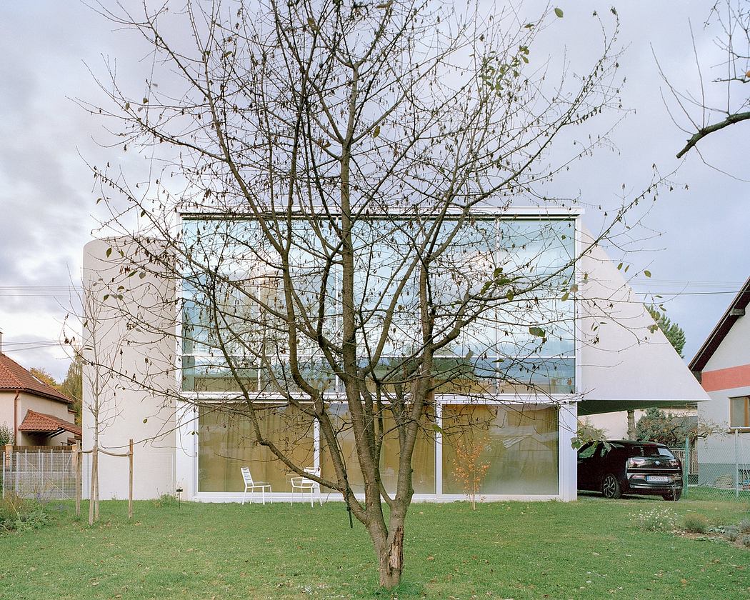 Sleek, modern glass building surrounded by a grassy yard and a bare tree in the foreground.