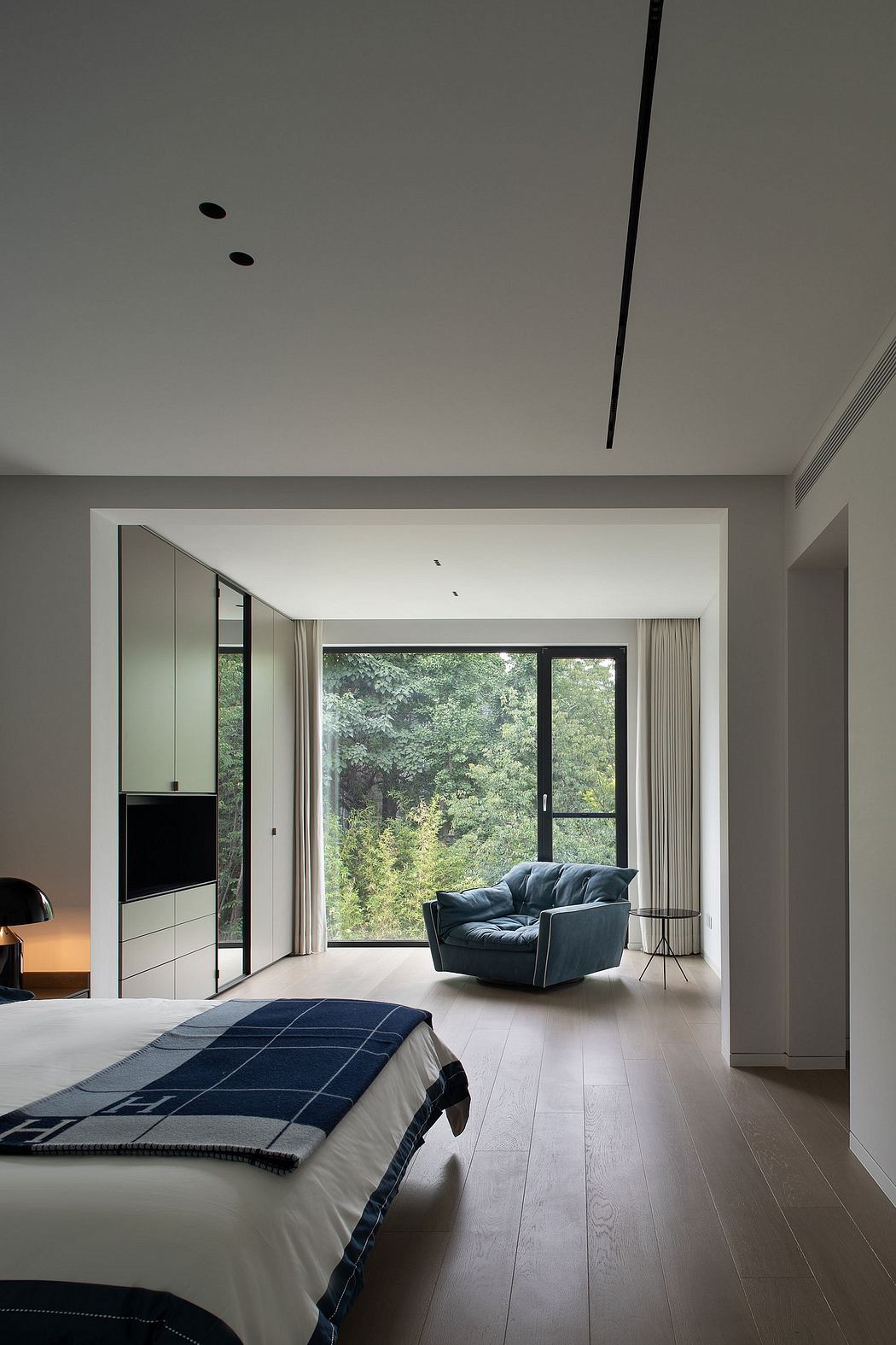 Spacious, modern bedroom with a cozy sitting area and large windows overlooking greenery.