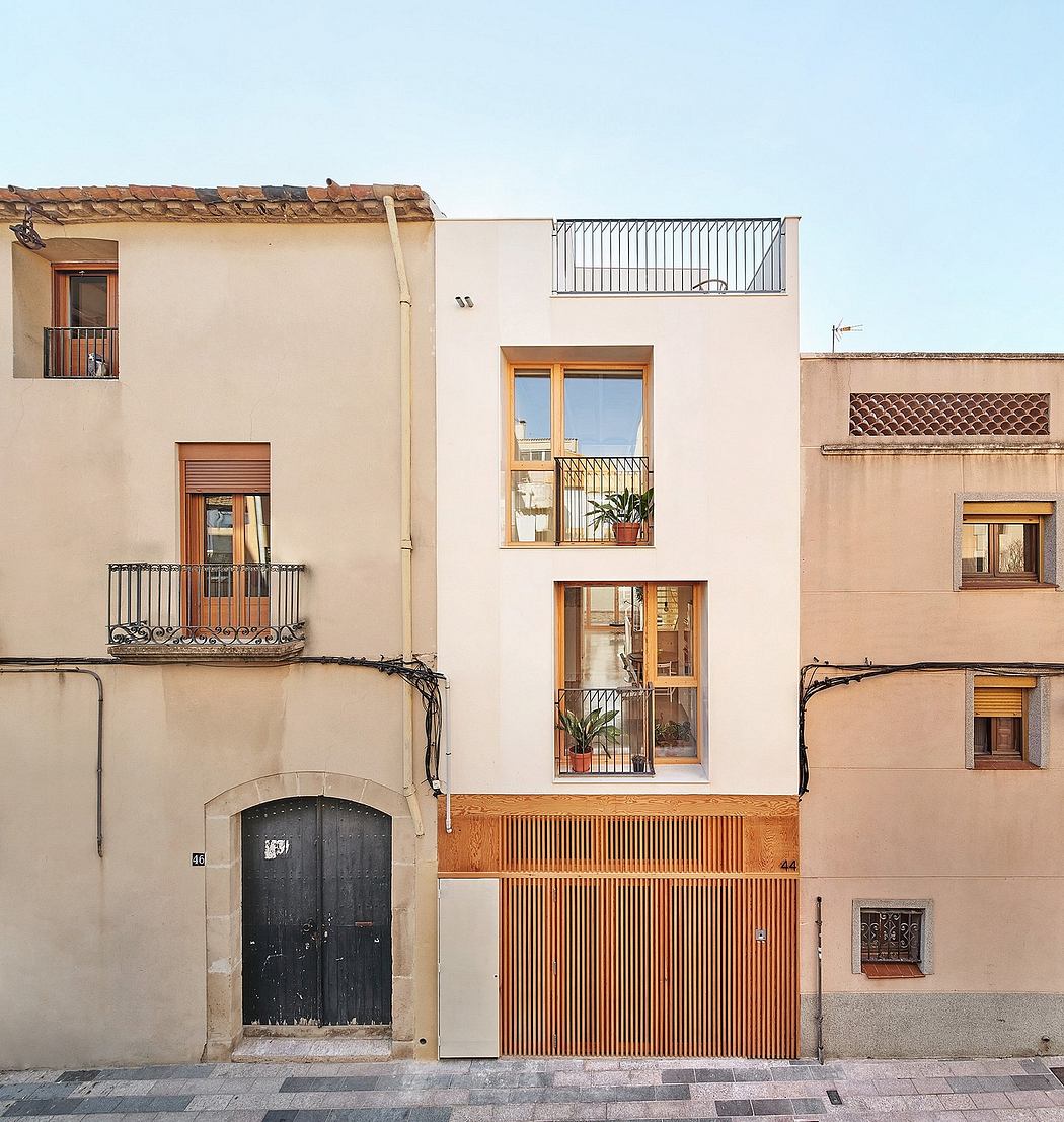 A charming Spanish-style building with a wooden balcony, ornate windows, and a black wooden door.