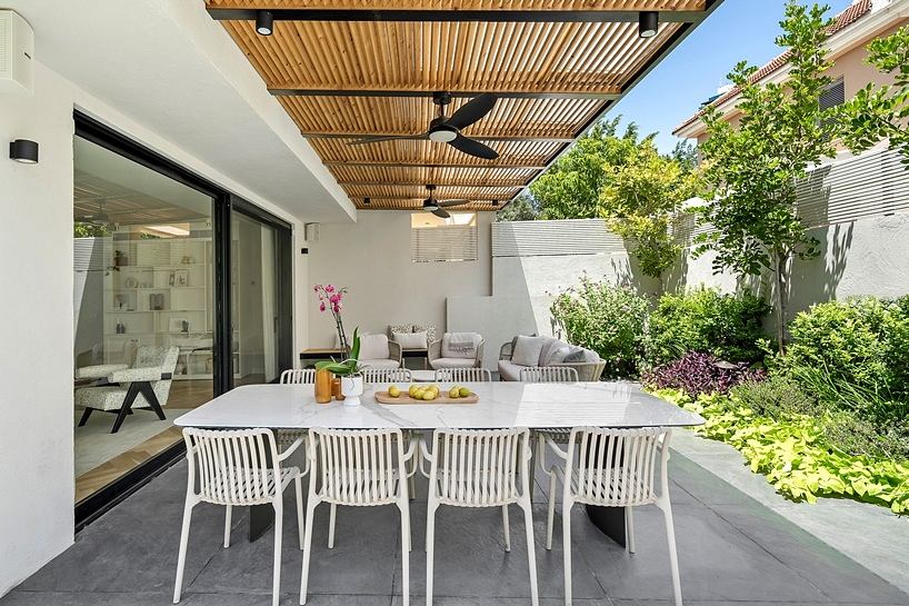 Outdoor patio with a wooden pergola overhead, modern furniture, and lush landscaping.