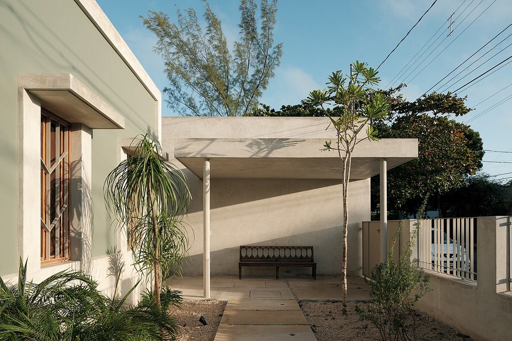 A modern concrete structure with a covered patio, lush greenery, and a bench.