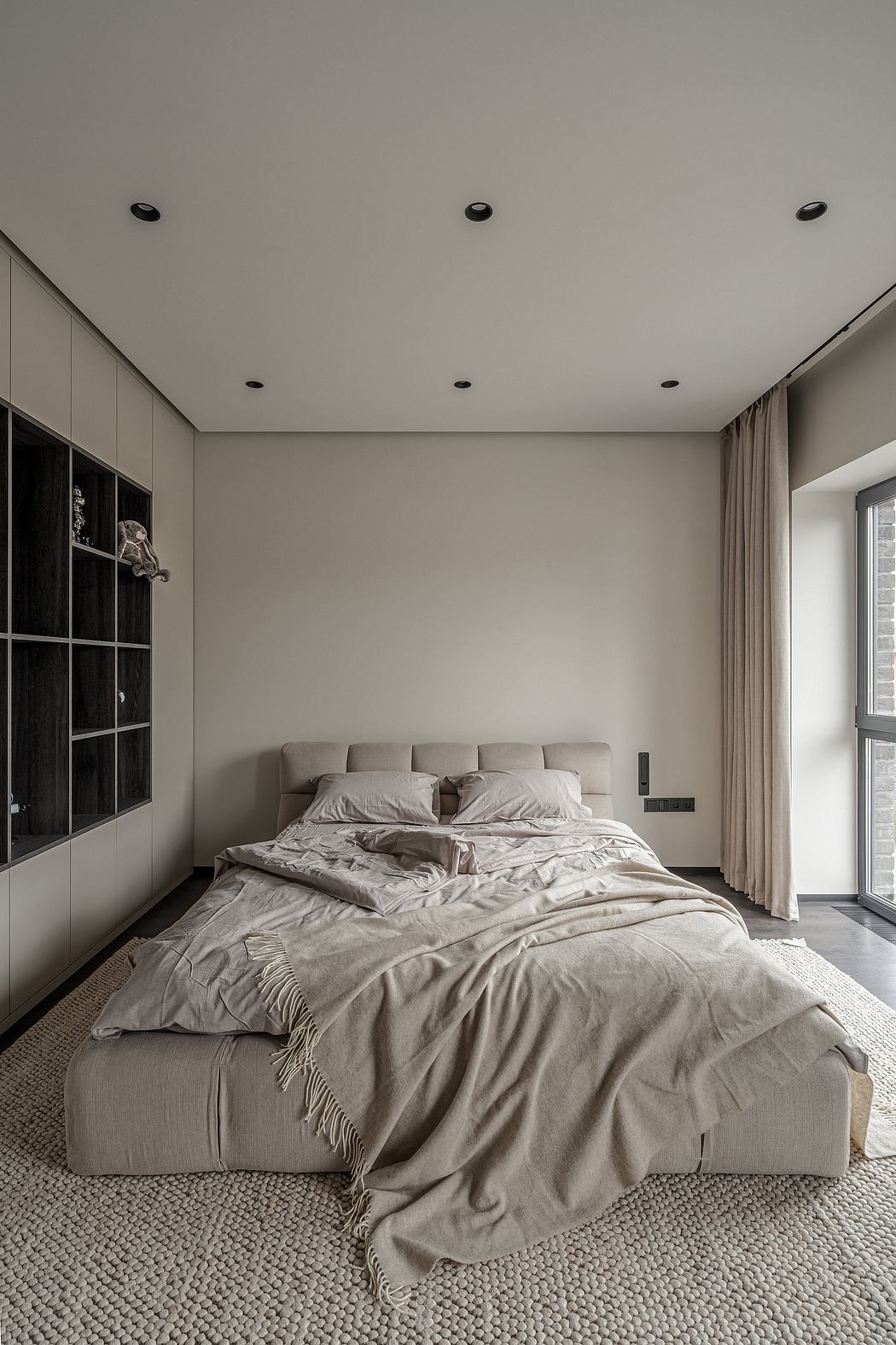 Minimalist bedroom with neutral color palette, recessed lighting, and textured flooring.