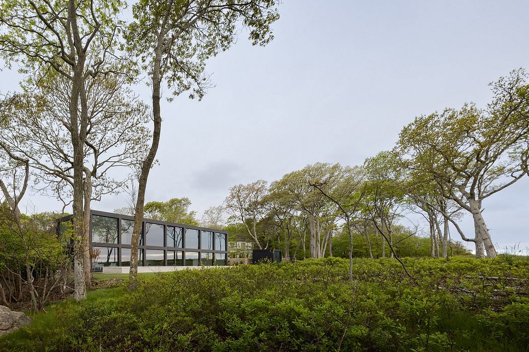 A modern glass structure set amidst lush greenery and mature trees.