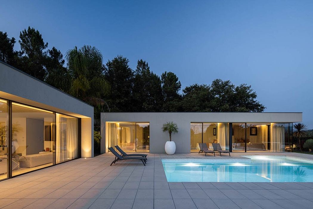 Sleek modern poolside retreat with glass walls, lush greenery, and inviting loungers.