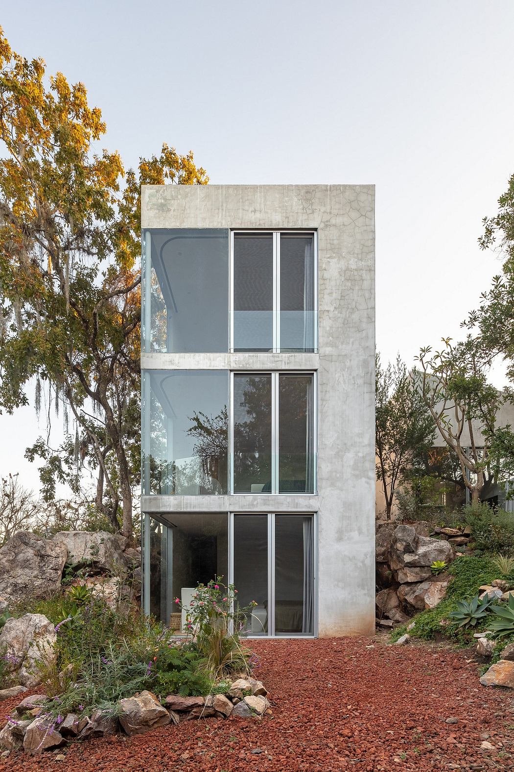 A modern, multi-story concrete structure with large windows surrounded by lush landscaping.