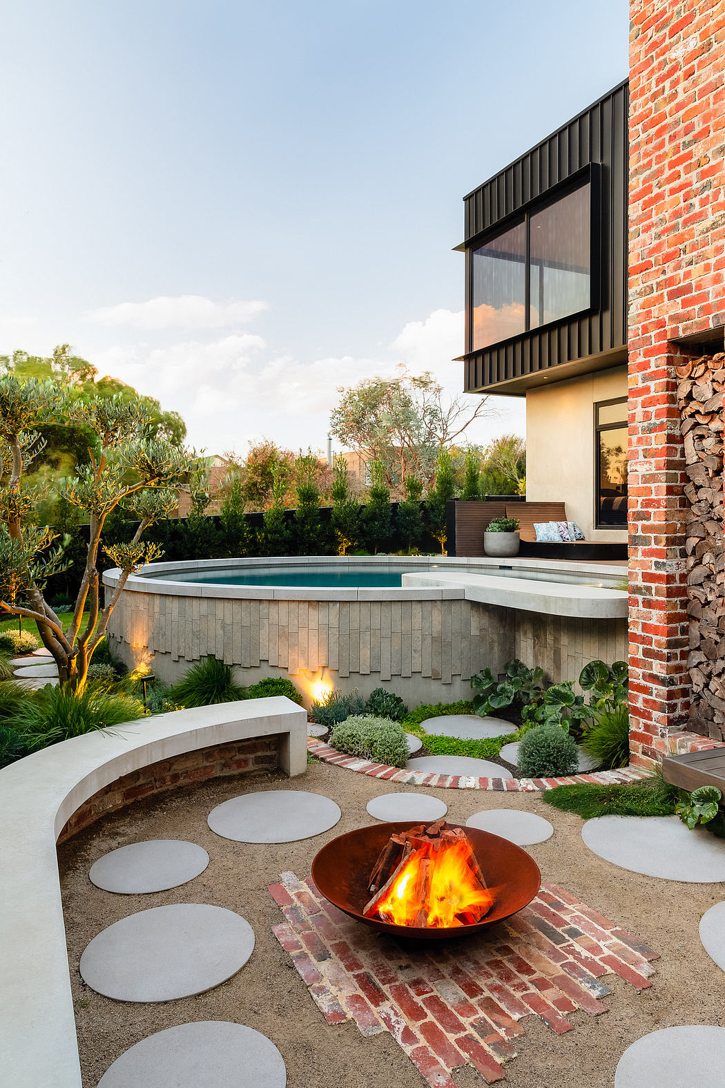 Sleek modern architecture with a cozy outdoor fire pit and circular pool surrounded by lush greenery.